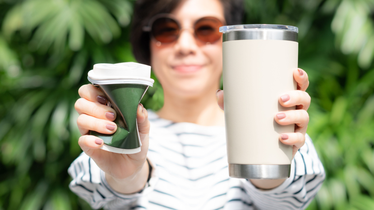 6 Things Frugal People Always Swap To Save Money 2 A stylish beautiful woman holding takeaway coffee cup in both hands, one is a single use paper cup with plastic lid the other one is a reusable stainless tumbler. Say no to plastic, No straw, 0 waste.