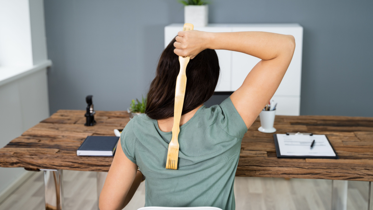 Young Woman Using Back Scratcher At Office