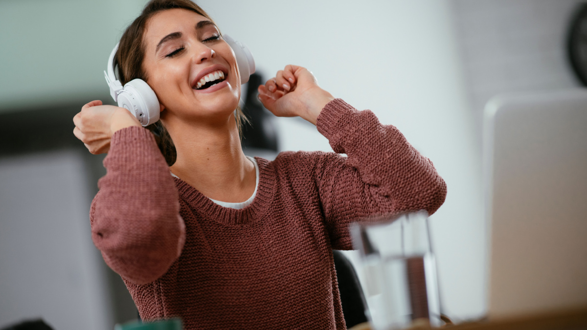 Young woman in office with headphones. Young casual businesswoman enjoying in her favorite song over headphones and singing while working on laptop in the office.