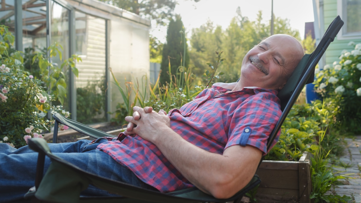 Adult man in casual clothing sitting in a deck chair and resting having a nap on summer day.