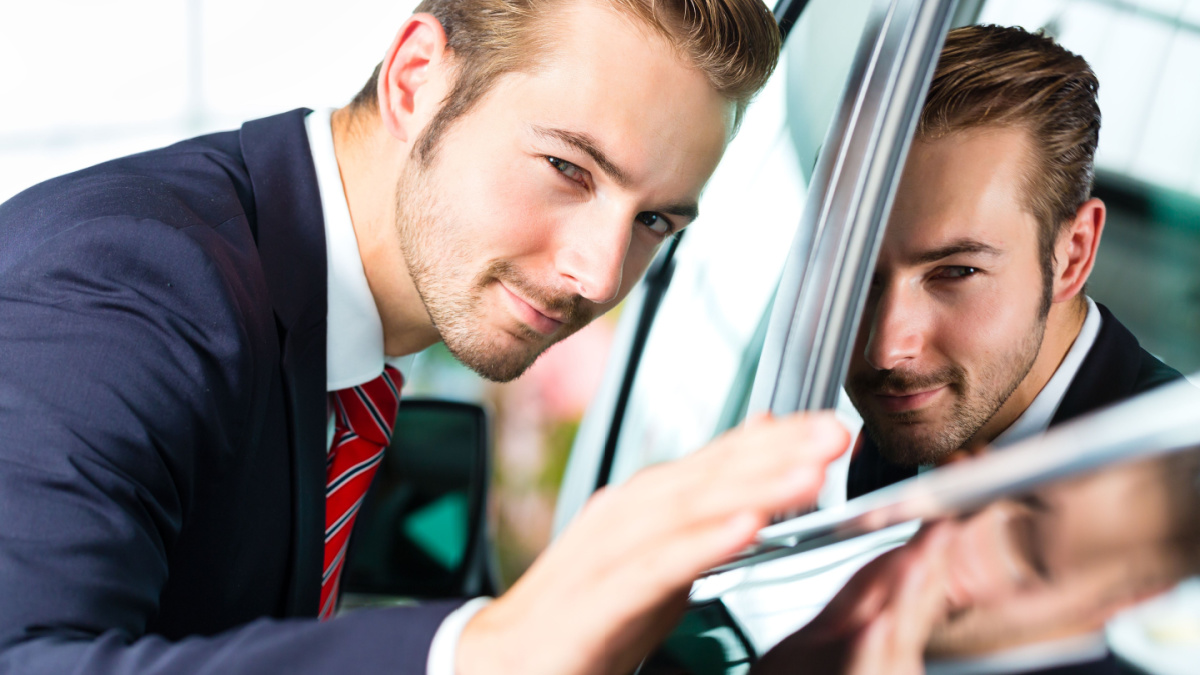 Seller or car salesman in car dealership presenting the reflecting car paint of his new and used cars in the showroom.