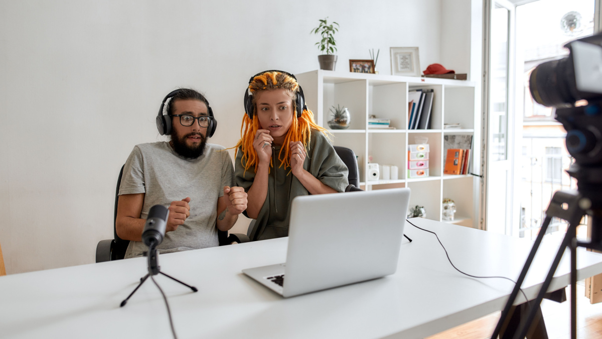 Couple of bloggers, young man and woman looking scared while watching something on laptop, recording reaction video blog or vlog
