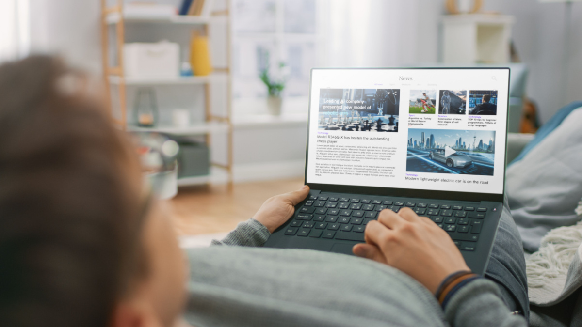 Young Man at Home Laying on a Couch and Using Laptop Computer for Reading News about Technological Breakthroughs.