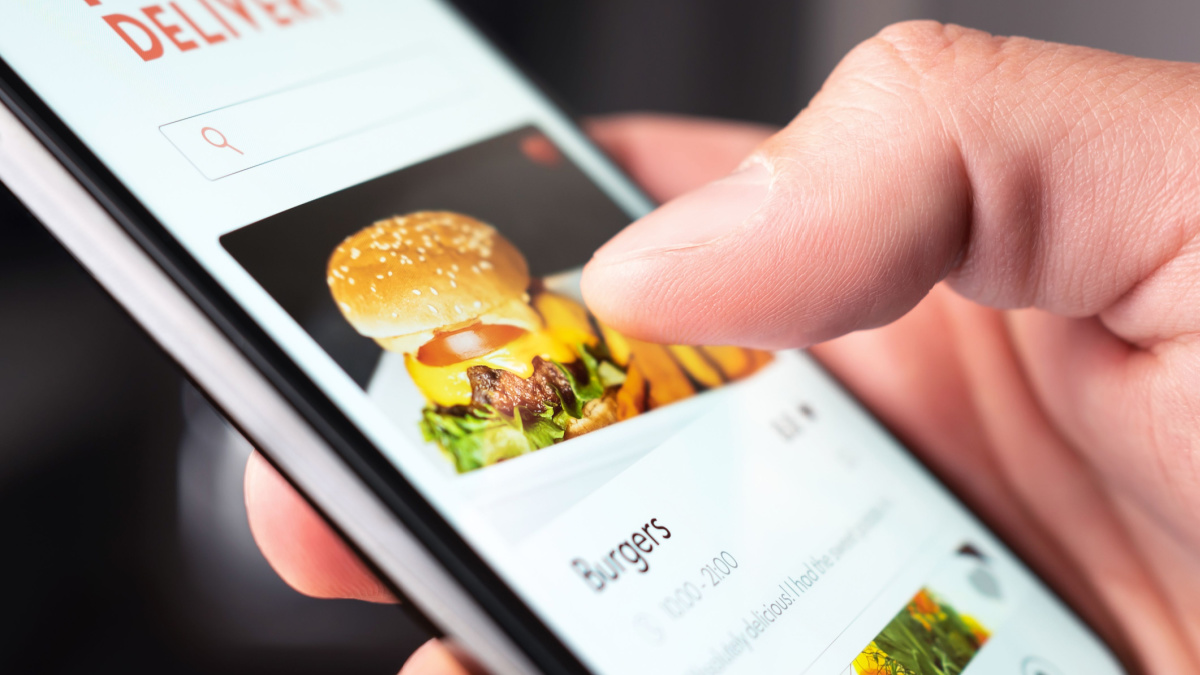 Food delivery app order with phone. Online mobile service for take away burger and pizza. Hungry man reading restaurant menu, website and reviews with smartphone. Takeout or fast courier deliver.