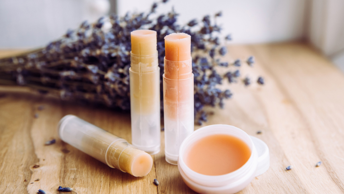 Make homemade natural organic ingredients lip balm. Handmade lip balm and lipstick inside container on natural wooden background and lavender for decoration.