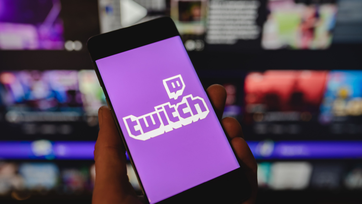 Twitch logo on smartphone in hand and the official website. Popular streaming service.