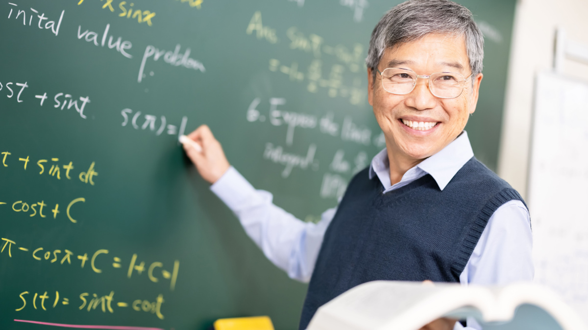 asian senior male calculus professor is writing on blackboard in the classroom at college.