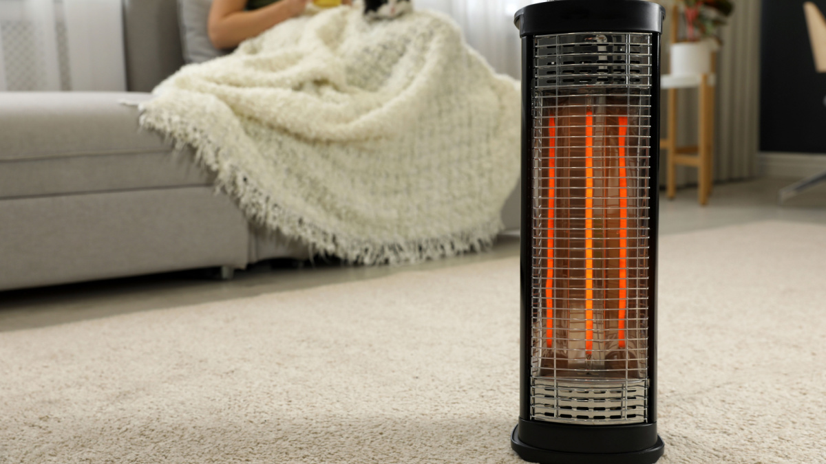 Woman with cat at home, focus on electric halogen heater, closeup.