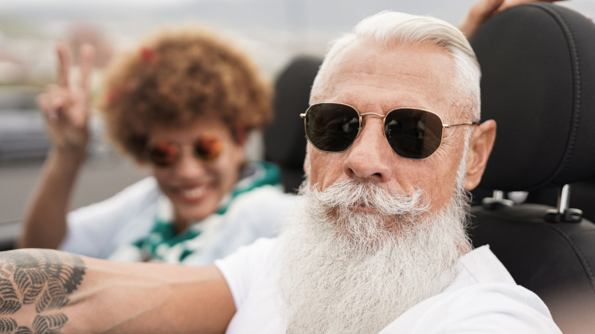 Multiracial senior couple taking selfie inside convertible car in summer vacation.