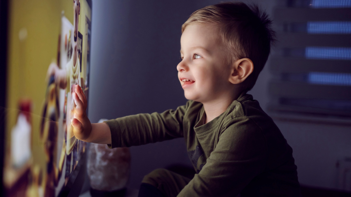 A bedtime ritual for toddlers. The boy touched the TV screen with one hand. A close-up shot of a kid in pajamas sitting right in front of the TV and staring at a cartoon Watching favorite cartoon show
