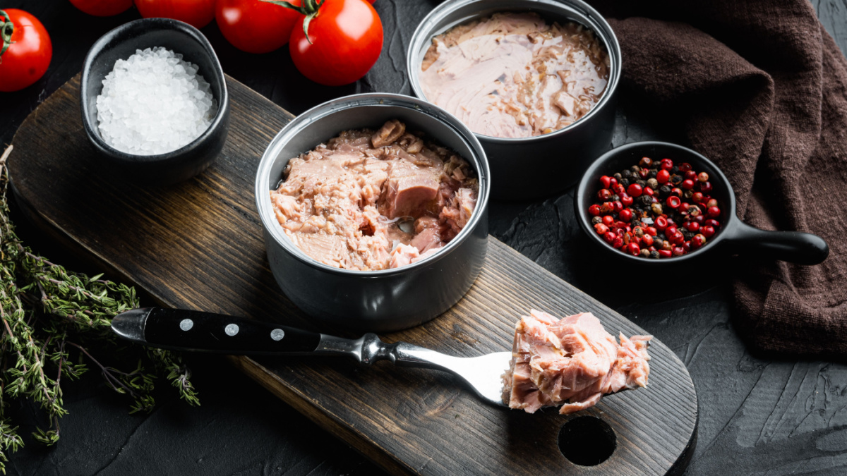 Canned tuna, fish preserves set, on wooden cutting board, on black background with herbs and ingredients