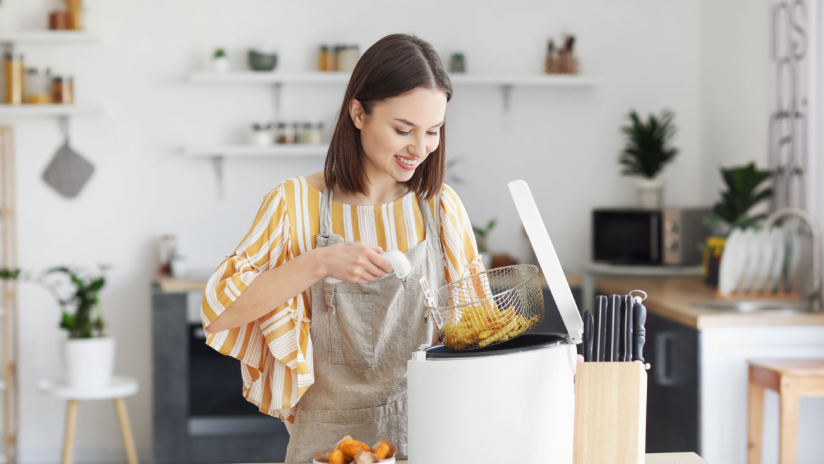 Young woman taking tasty french fries from deep fryer in kitchen
