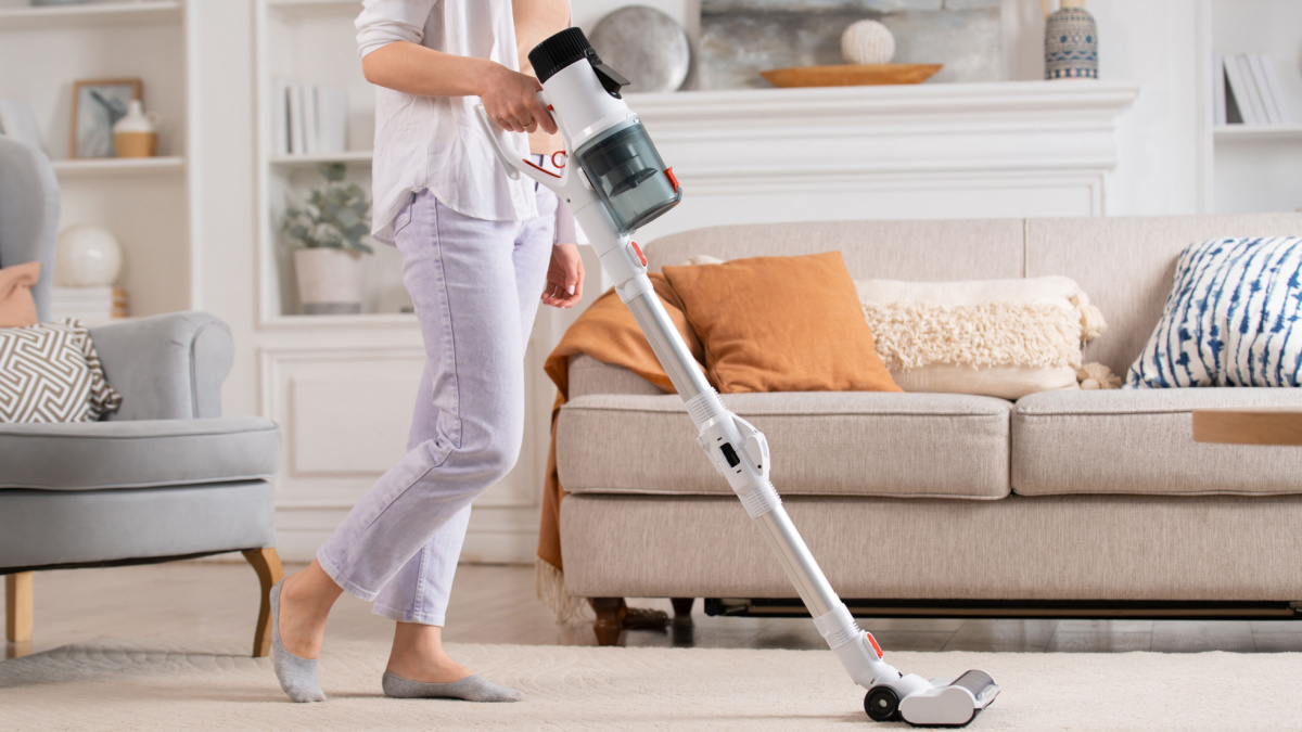 Young woman uses cordless vacuum cleaner to clean home carpet. Modern easy cleaning.