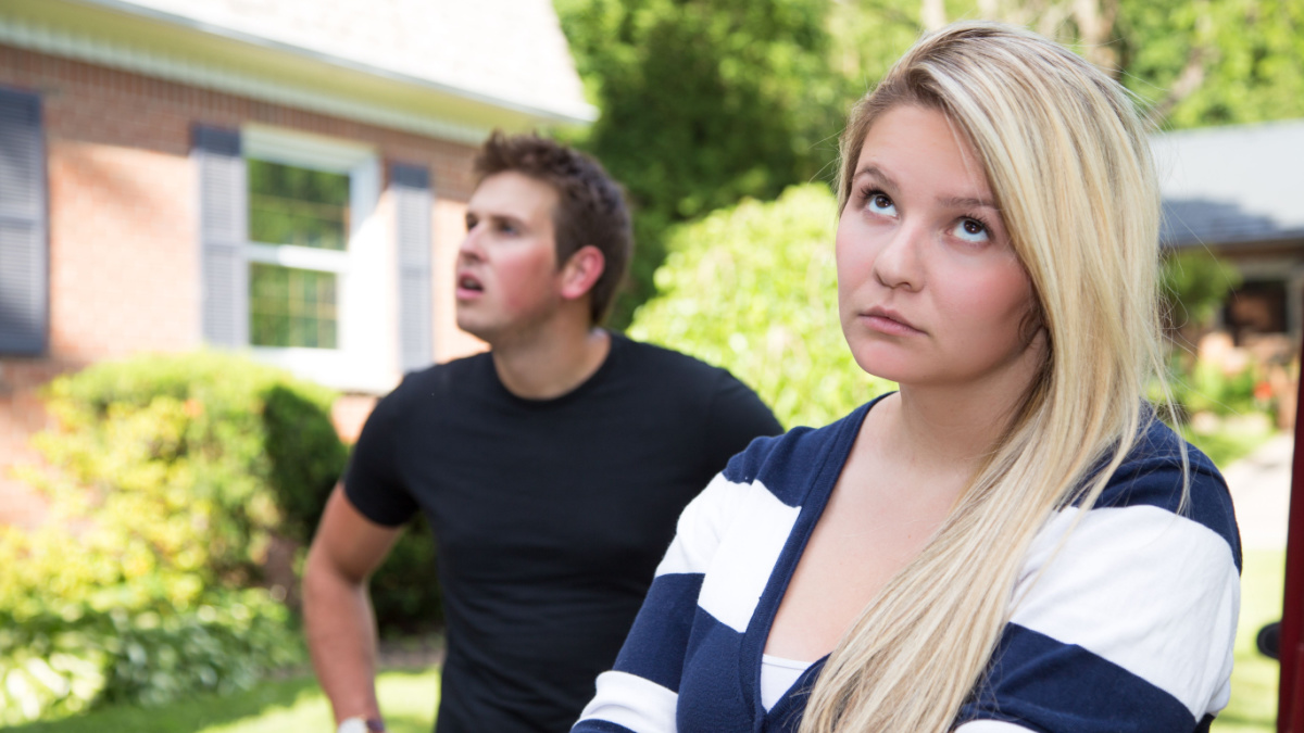 A young couple having a disagreement. The young lady rolls her eyes at the young man who seems distracted and confused in the background.