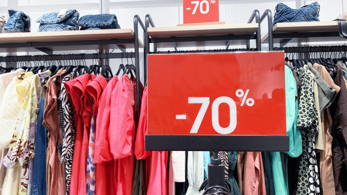 Red stand with big 70 percent discount price in shopping center. Advertising of Black Friday cheap clothes.Season sale concept with clothes hangers on background.