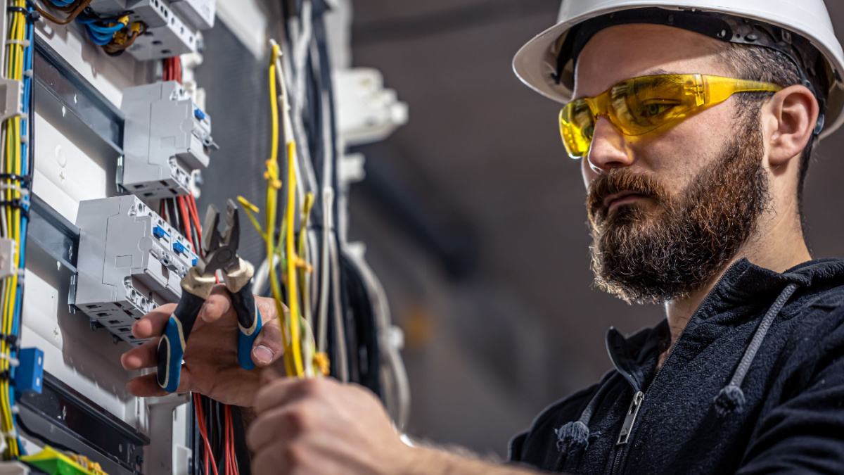 A male electrician works in a switchboard with an electrical connecting cable.