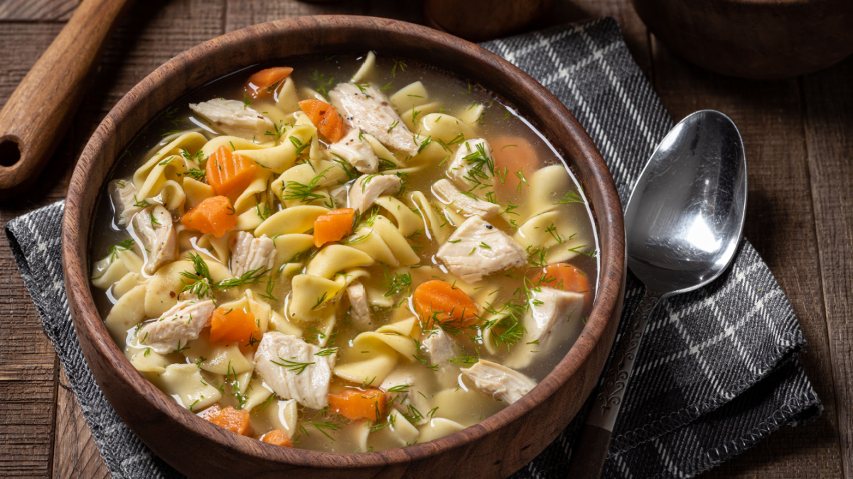 Bowl of chicken noodle soup with carrots and dill on a rustic wooden table