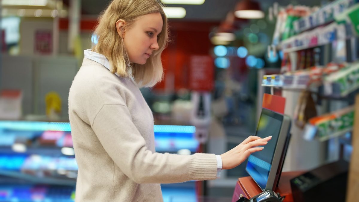 Woman pays at self-checkouts in supermarket.