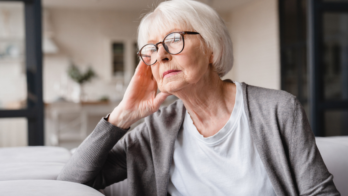 Sad tired ill sick lonely disappointed caucasian old elderly senior woman grandmother sitting on the sofa couch, feeling nostalgy, pain, missing grandchildren, bankruptcy, fraud at home.