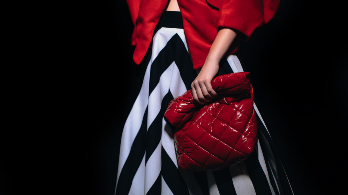 Female figure dressed in a stylish long striped black white skirt and red jacket holding leather creative handbag.