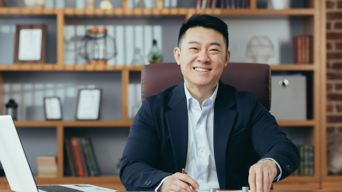 Portrait of a successful Asian banker, businessman working in the office, looking at the camera and smiling, counting metal coins on the table.