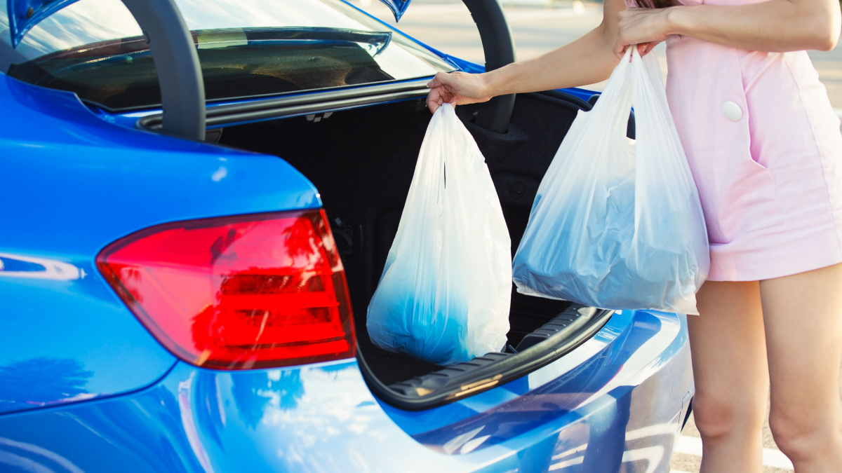 Cropped image of woman putting shopping bags inside trunk of her blue car, on a mall, store, supermarket parking lot.