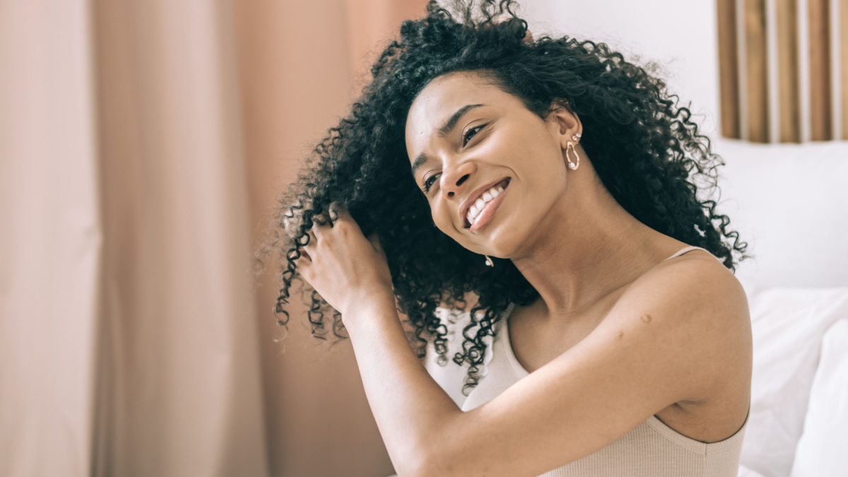 Curly girl method concept. Close up young african curly haired woman combing her hair in the bedroom. Hair care