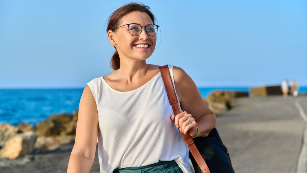 Beautiful mature woman with backpack walking outdoor on sea travel destination.