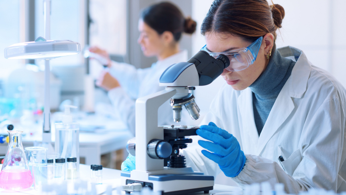 Young scientists conducting research investigations in a medical laboratory, a researcher in the foreground is using a microscope