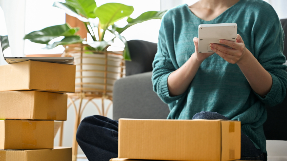 Female online seller using calculator to calculate the delivery fee for her packages.