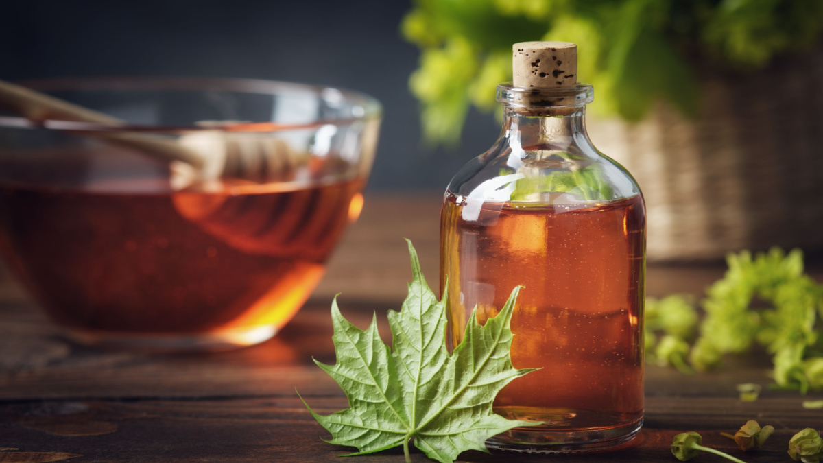 Bottle of maple syrup or healthy tincture and spring maple leaf. Bowl of maple syrup and wooden dipper on background.