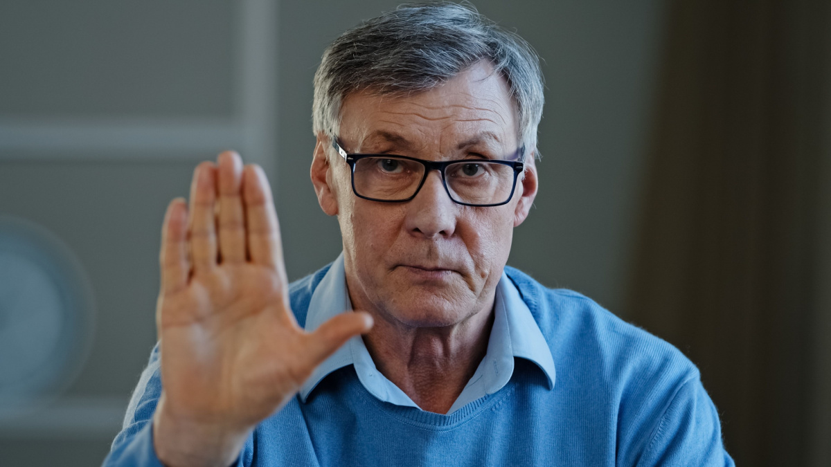 Serious old senior mature 60s man stretch out palm to camera says stop gesture indoors. Social problems older generation disrespect ban refusal disagreement. Aged businessman trouble denial rejection.