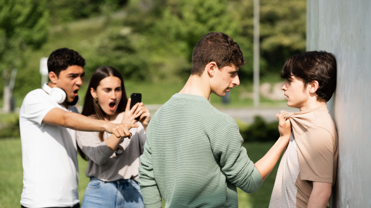 Teenager bully menacing boy while friends are recording. Bullying and violence at school concept
