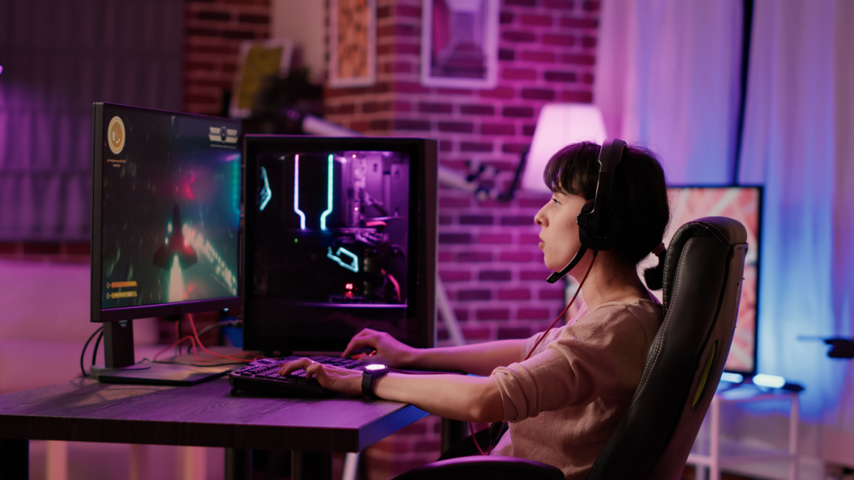Caucasian gamer girl relaxing playing fast paced space shooter simulation on professional pc setup while talking using gaming headset.