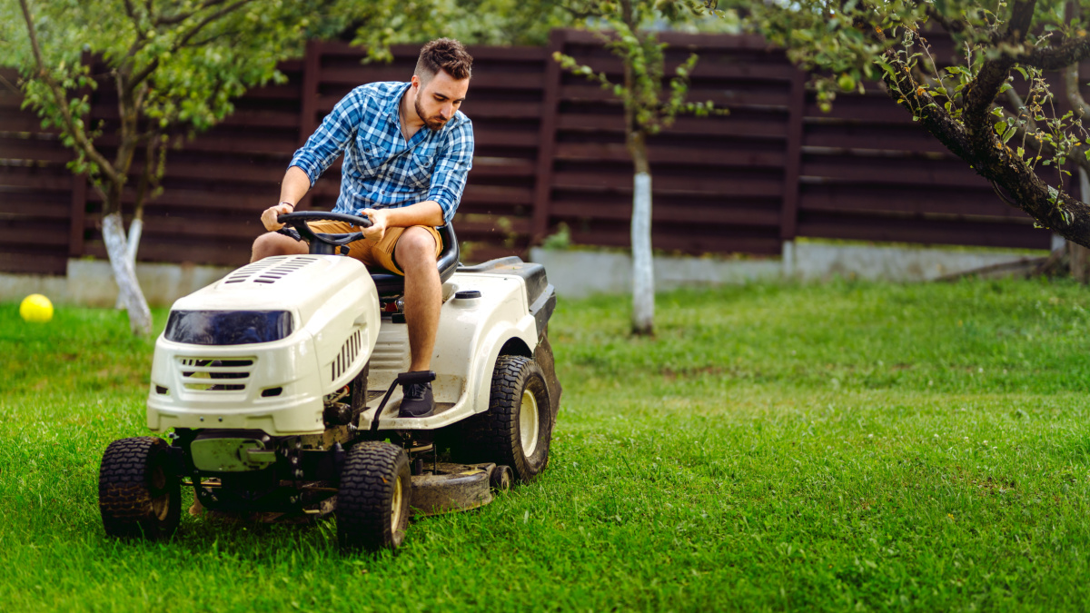 Professional gardener and lawn mower cuts the grass using tractor. Industrial landscaping works