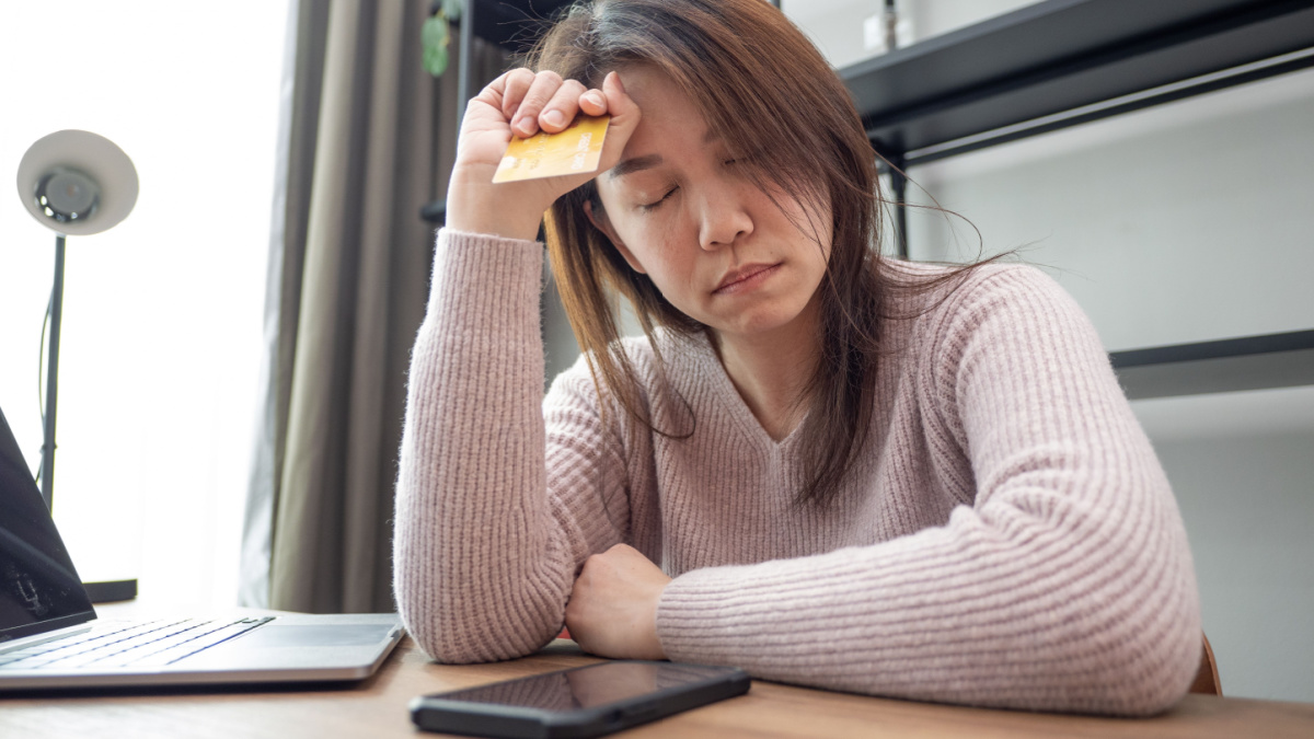Anxious woman using laptop and holding credit card feeling worried about finance problems at home.