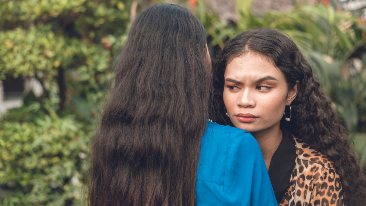 An insincere asian woman pretending to hug and comfort her friend, but in reality is annoyed and despises her.