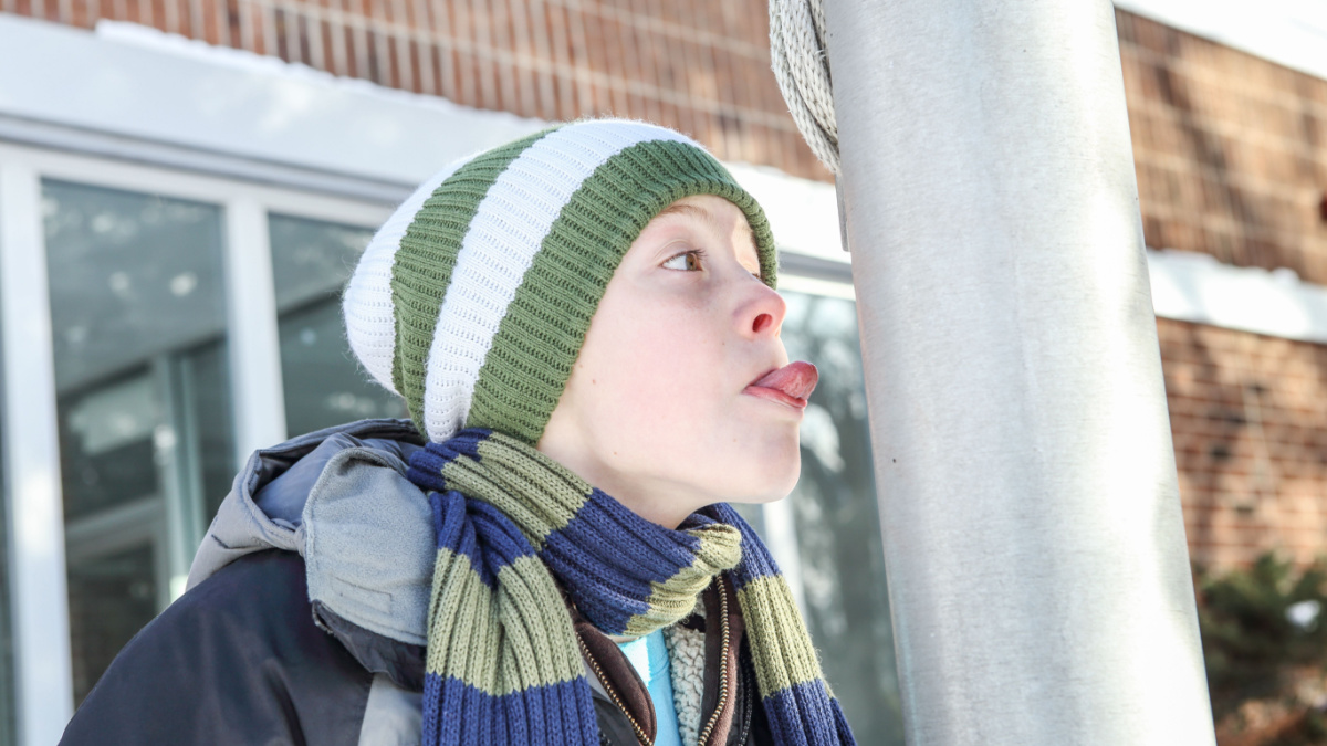 Boy sticking his tongue to a flag pole