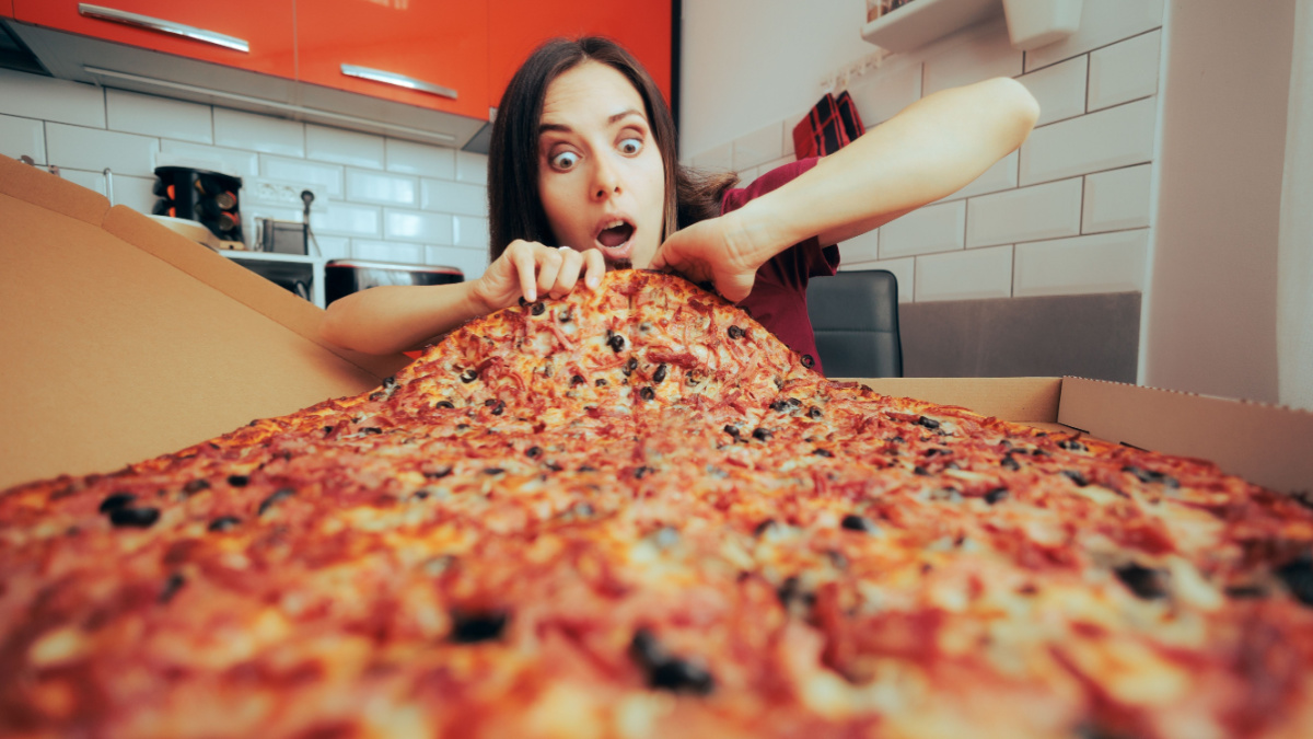 Hungry Woman Eating a Large Pizza by Herself in the Kitchen. Girl craving for a huge portion of Italian delicious dish