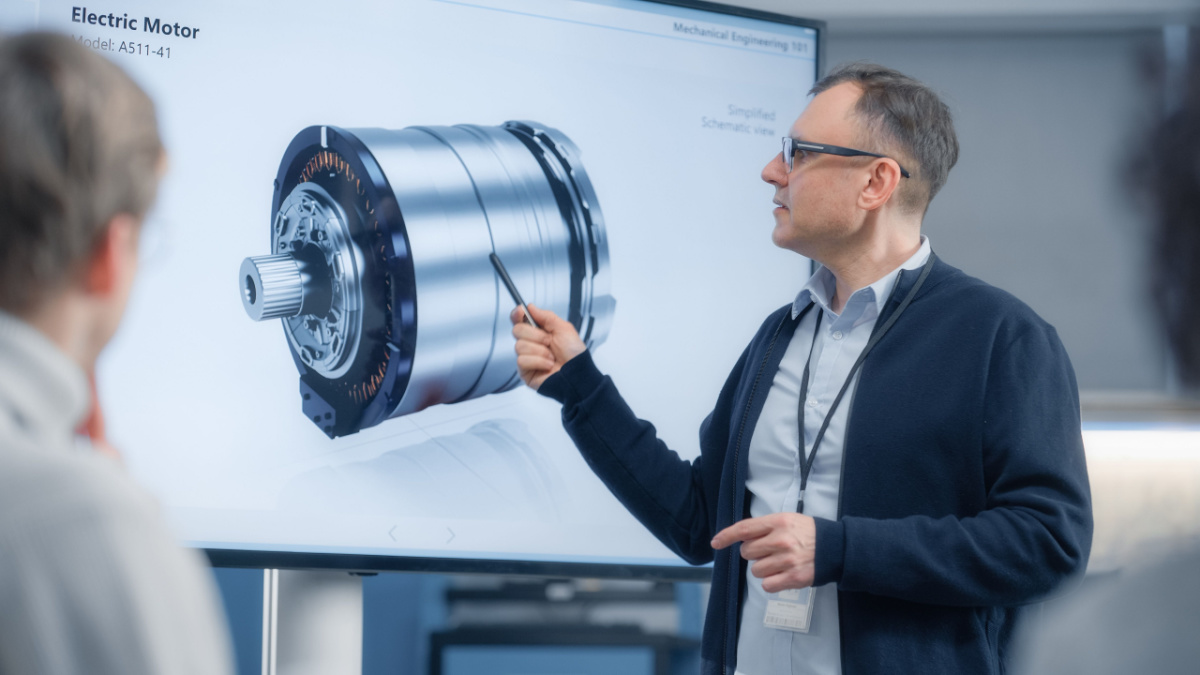 Male Chief Engineer Talks to Young Specialists About Components of the Electric Motor and Using Big Screen.