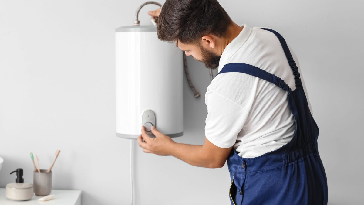 Male plumber adjusting boiler in bathroom.