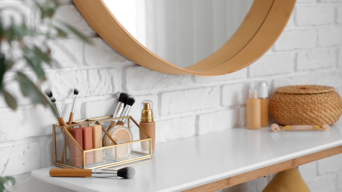 Organizer with makeup brushes and decorative cosmetics on table near white brick wall.