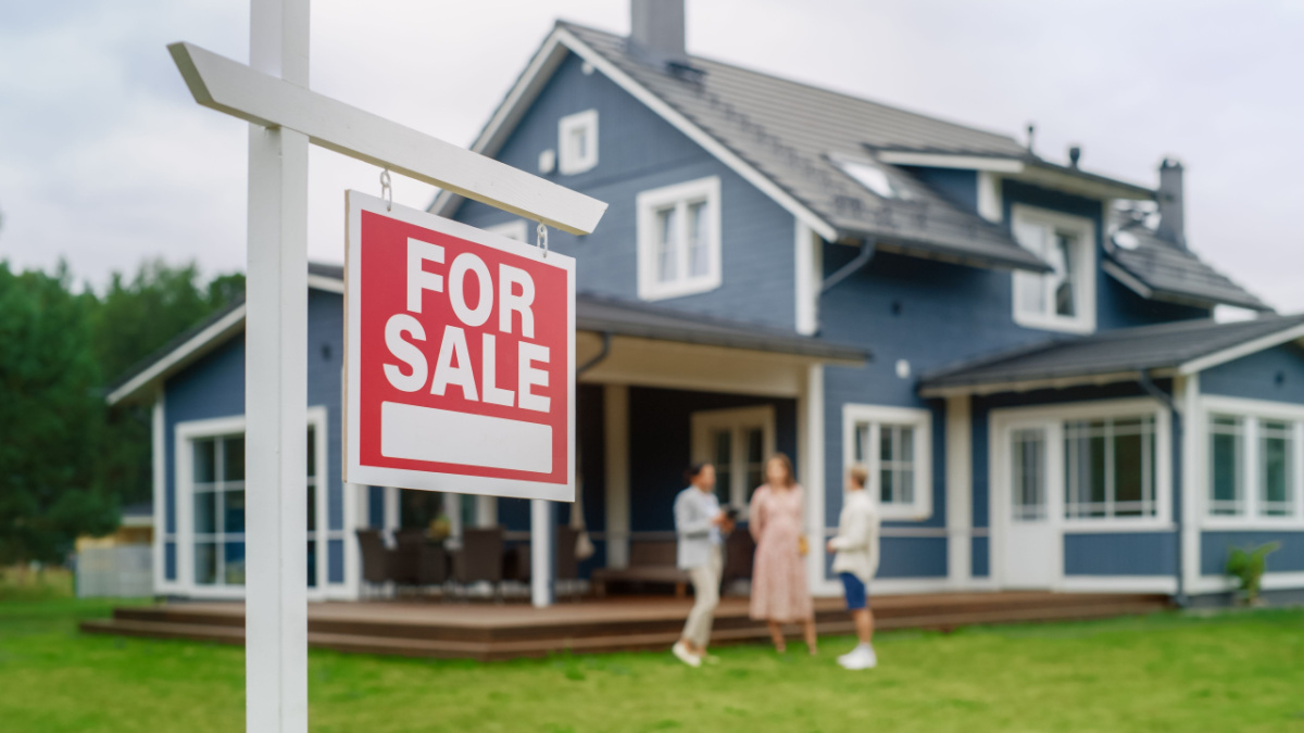 Young Couple Visiting a Potential New Home Property with Professional Real Estate Agent. Female Realtor Showing the Area to Future Homeowners. Focus on For Sale Sign.