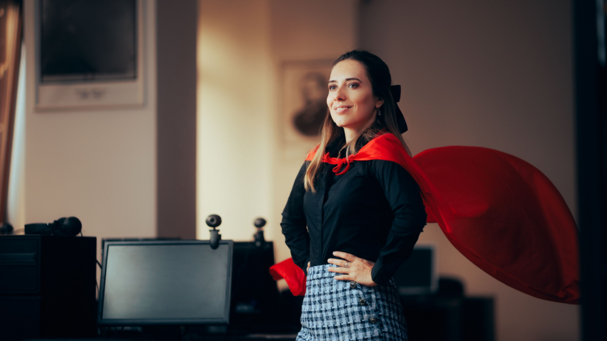 Happy Superhero Businesswoman Wearing a Red Cape in the Office Super heroine female manager showing strength and confidence