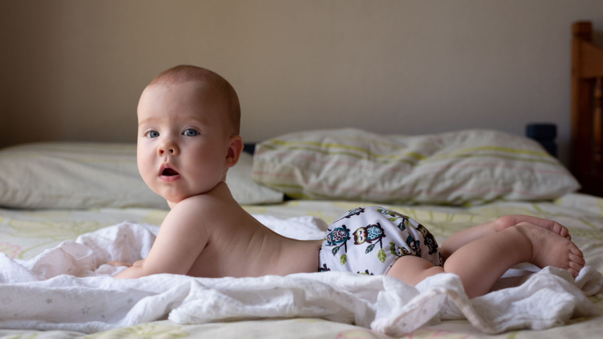 A happy, content baby girl lying on her stomach doing tummy time to strengthen her back muscles. She is wearing a modern, reusable cloth diaper.