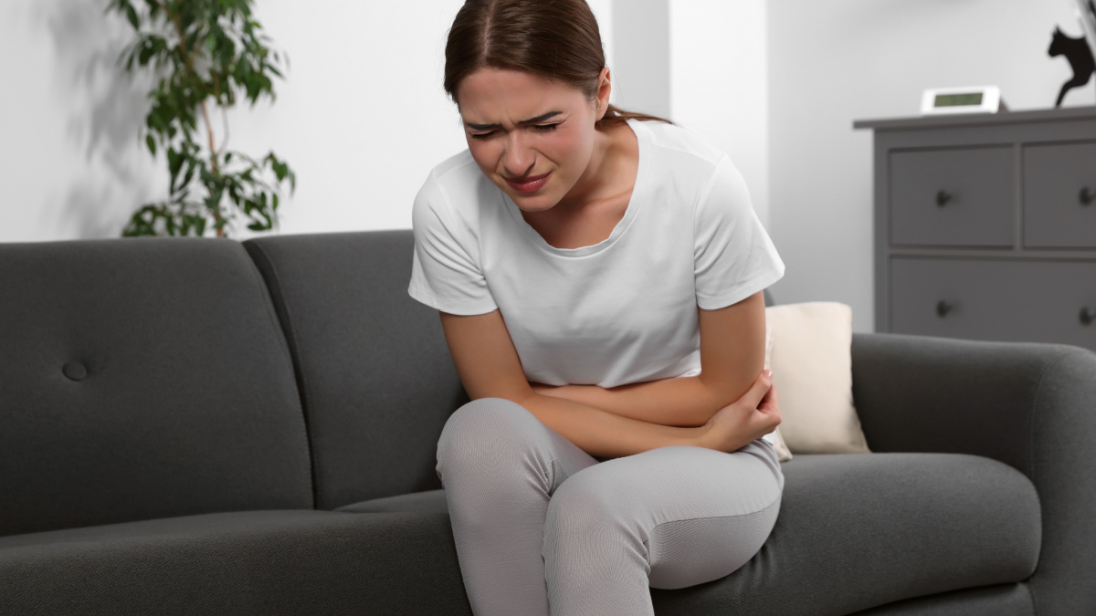 Young woman suffering from cystitis on sofa at home