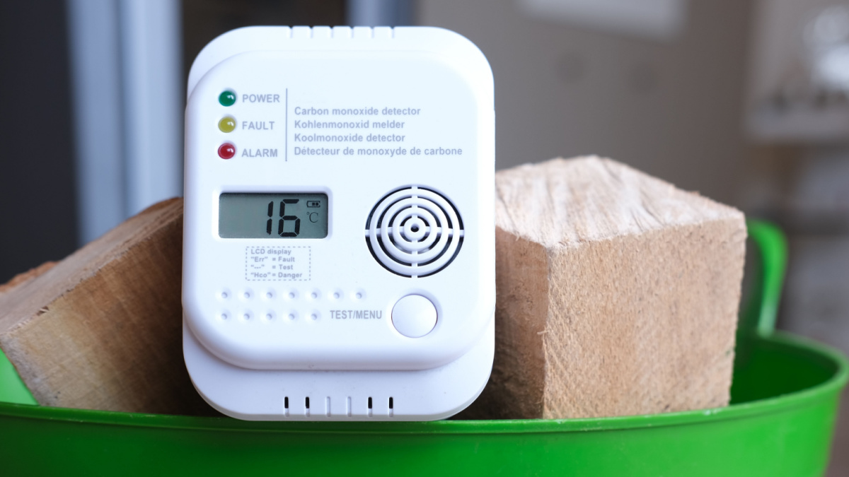 Detail shot of a carbon monoxide alarm or CO warning device in a basket of firewood in an apartment in front of a fireplace