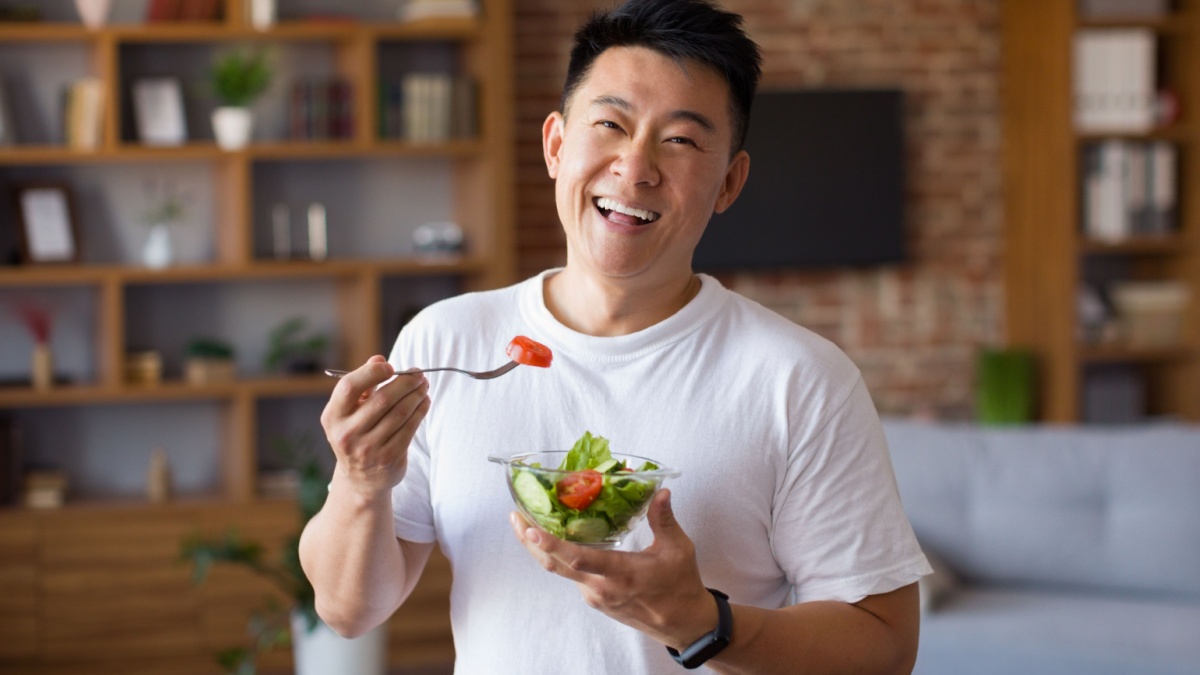 20 Essential Habits for a Longer, Healthier Life 10 Happy asian mature man holding fork and bowl with fresh vegetable salad, eating healthy lunch after domestic training. Active middle aged male having balanced meal.