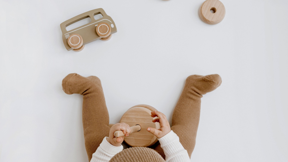 Little baby in stylish clothes plays with wooden toys. Fashion Scandinavian newborn clothes and toys.