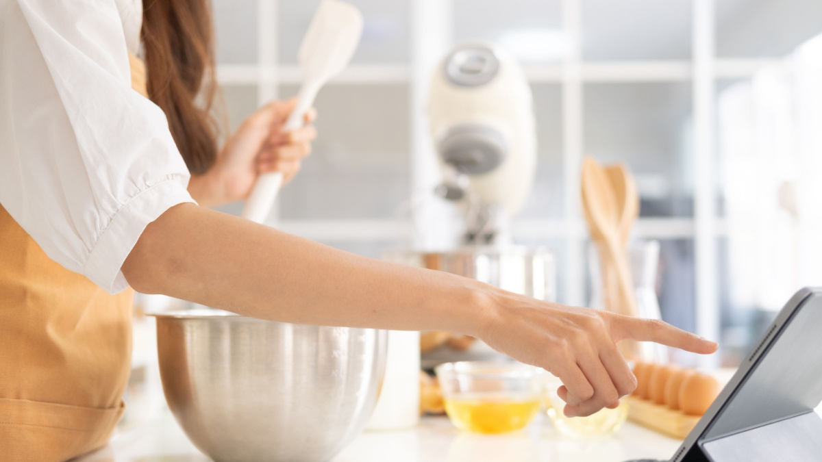 Close up of hands with computer in kitchen.Learn cooking online. A young woman is watching cooking tutorial video in the kitchen.Reading recipe while making cookies Following Recipe On Digital Tablet.